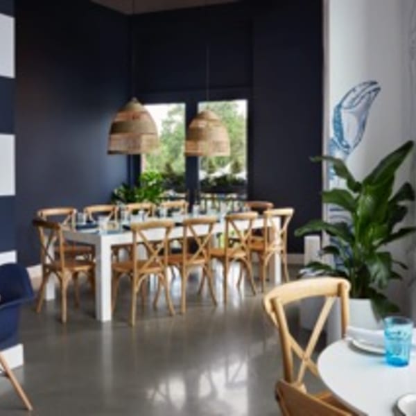 Lena's Wood-Fired Pizza & Tap dining room with long white table, wooden chairs, and woven pendant lights.