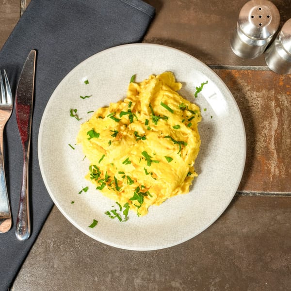 A plate of fluffy scrambled eggs topped with fresh parsley, next to silverware and salt and pepper shakers.