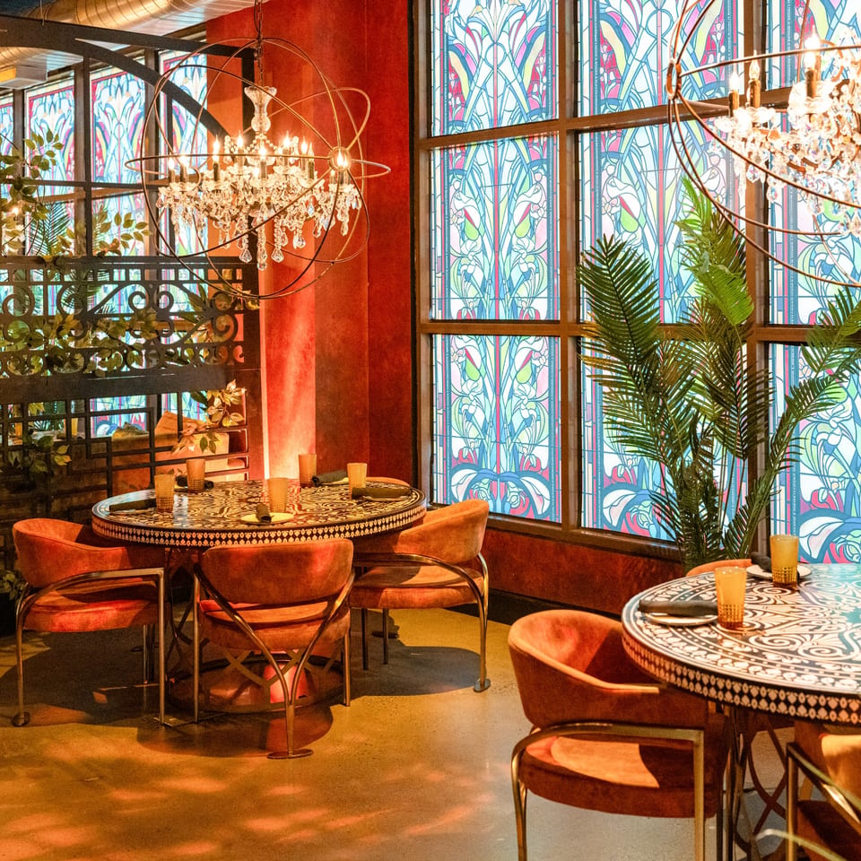 Lena's Wood-Fired Pizza & Tap dining area with ornate tables, orange chairs, chandeliers, and stained glass windows.