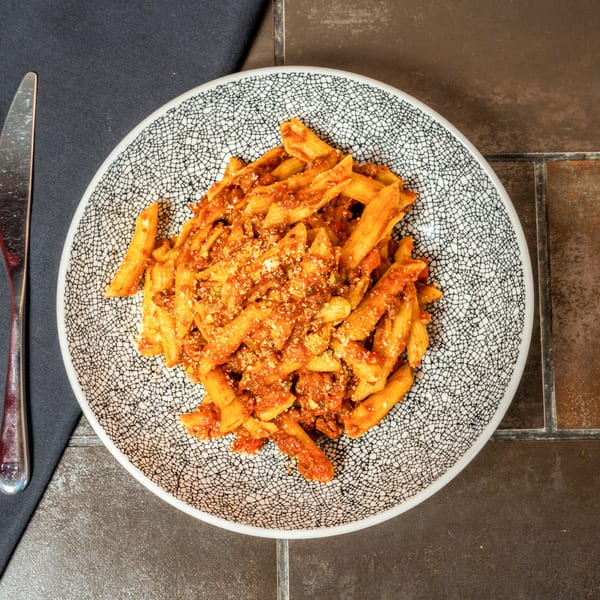 Penne pasta with rich red sauce and grated cheese in a patterned bowl, next to a fork.