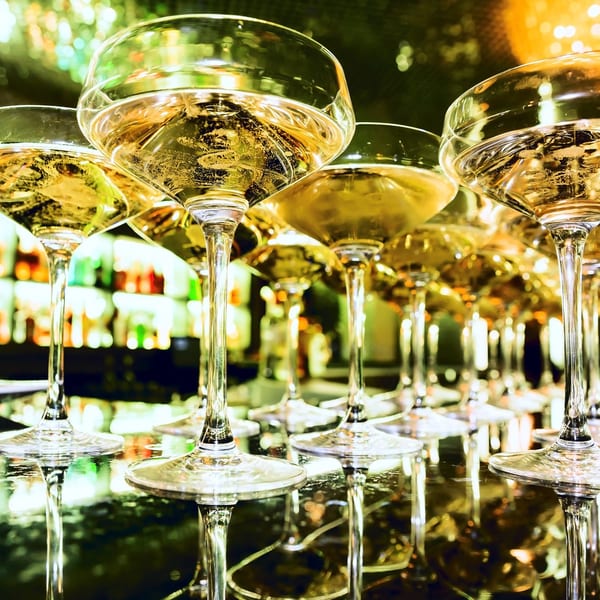 Row of champagne coupes filled with sparkling wine, reflecting the bar lights at Lena's.