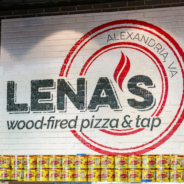 Lena's Wood-Fired Pizza & Tap logo on a white brick wall above rows of tomato cans.