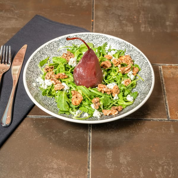 Arugula salad with a poached pear, candied walnuts, and crumbled blue cheese in a patterned bowl.