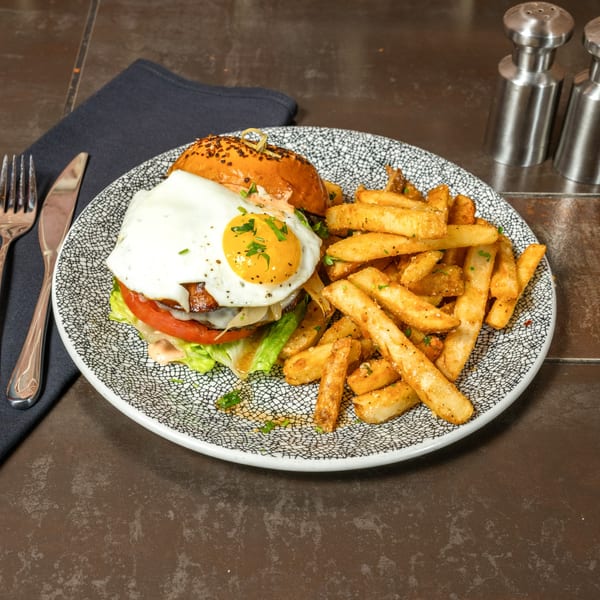 Lena's burger with a fried egg, lettuce, tomato, and fries on a patterned plate.