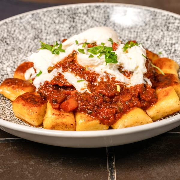 Lena's Wood-Fired Pizza & Tap's gnocchi with red sauce, burrata, and fresh herbs in a patterned bowl.